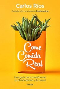 Portada del libro 'Come Comida Real' de Carlos Ríos, destacando un vibrante fondo naranja con un paquete ilustrado que contiene judías verdes, simbolizando la esencia de una alimentación saludable y natural