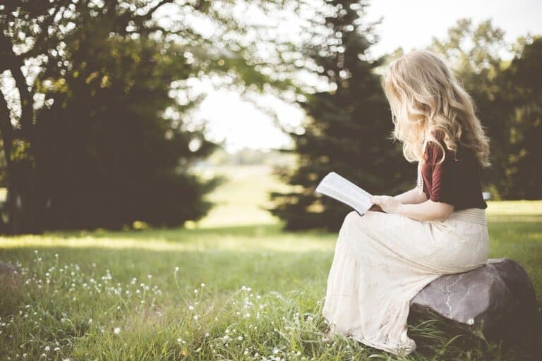 Niña rubia leyendo en la naturaleza, sentada sobre una piedra, capturada por 'Es de Leer'.